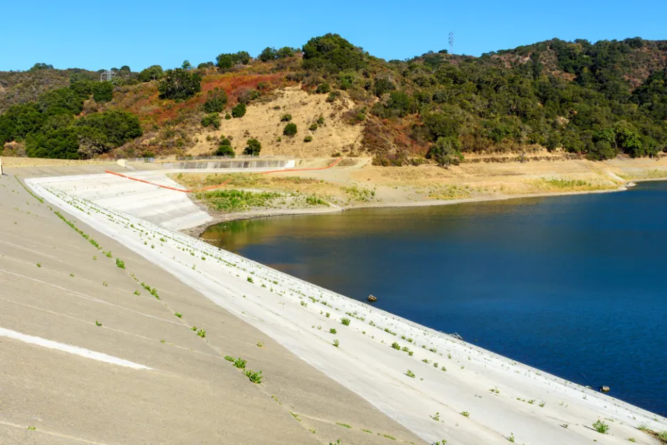 Concrete dam of almost dried, low water level Stevens Creek reservoir in San Francisco Bay Area, California.